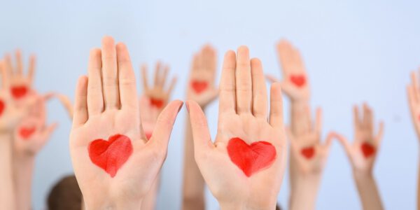 Hände sind in die Luft gestreckt, auf den Handinnenflächen sind mit Farbe rote Herzen gemalt Hände sind in die Luft gestreckt, auf den Handinnenflächen sind mit Farbe rote Herzen gemalt