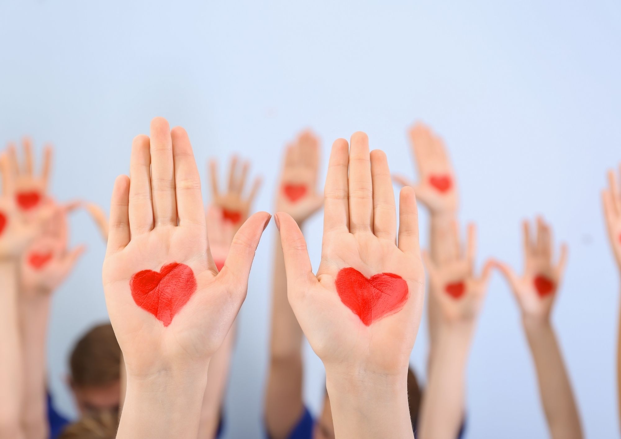 Hände sind in die Luft gestreckt, auf den Handinnenflächen sind mit Farbe rote Herzen gemalt