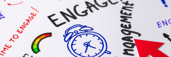 Auf einem Blatt Papier steht mehrmals in bunter und großer Schrift das Wort Engagement mit einem Wecker Auf einem Blatt Papier steht mehrmals in bunter und großer Schrift das Wort Engagement mit einem Wecker