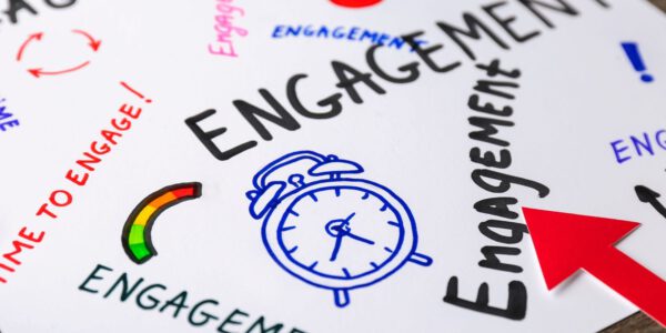 Auf einem Blatt Papier steht mehrmals in bunter und großer Schrift das Wort Engagement mit einem Wecker