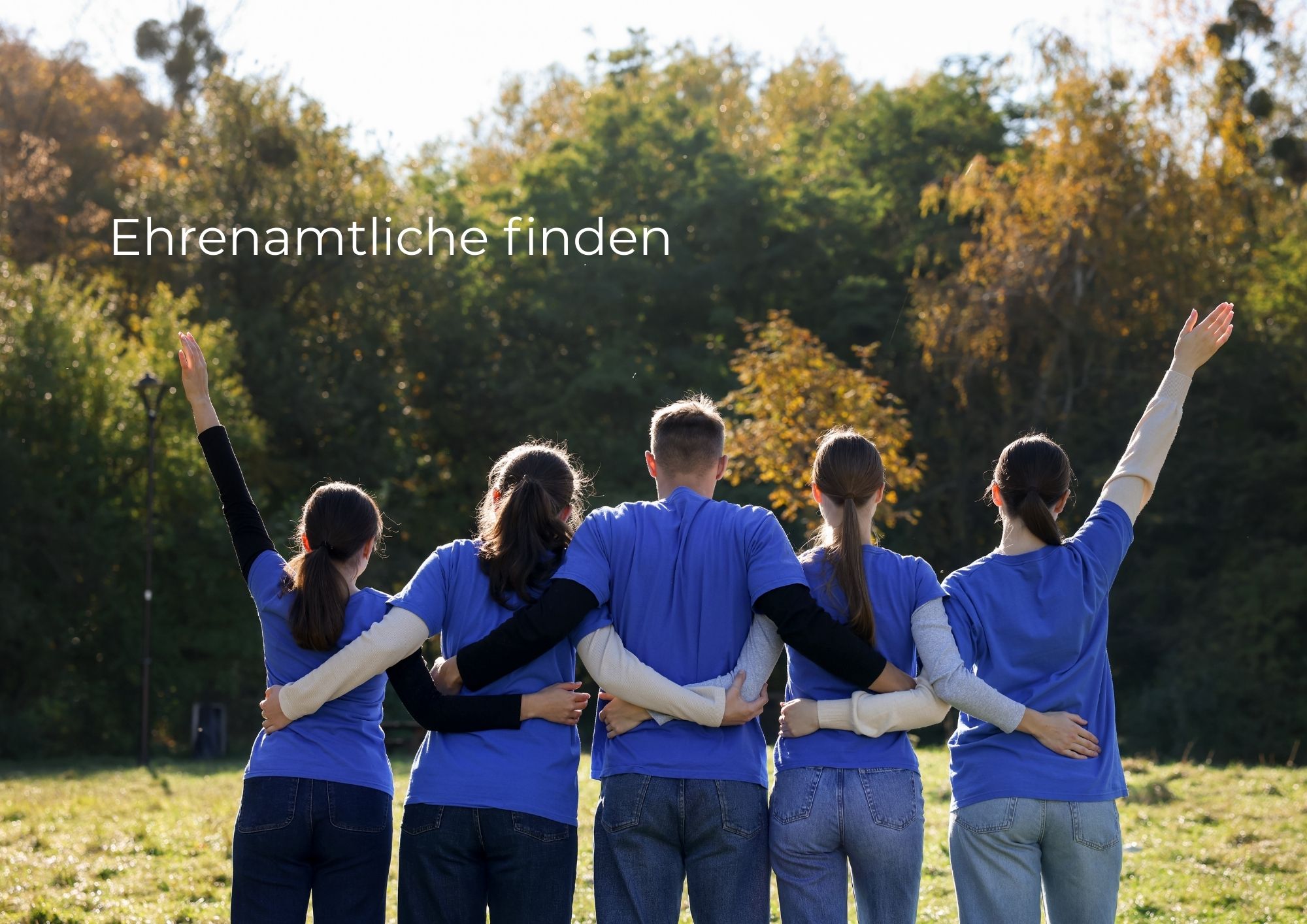 Gruppe von fünf Personen in blauen Shirts steht auf einer Wiese und schaut in Richtung Wald, mit erhobenen Armen; Text „Ehrenamtliche finden“ steht links im Bild.