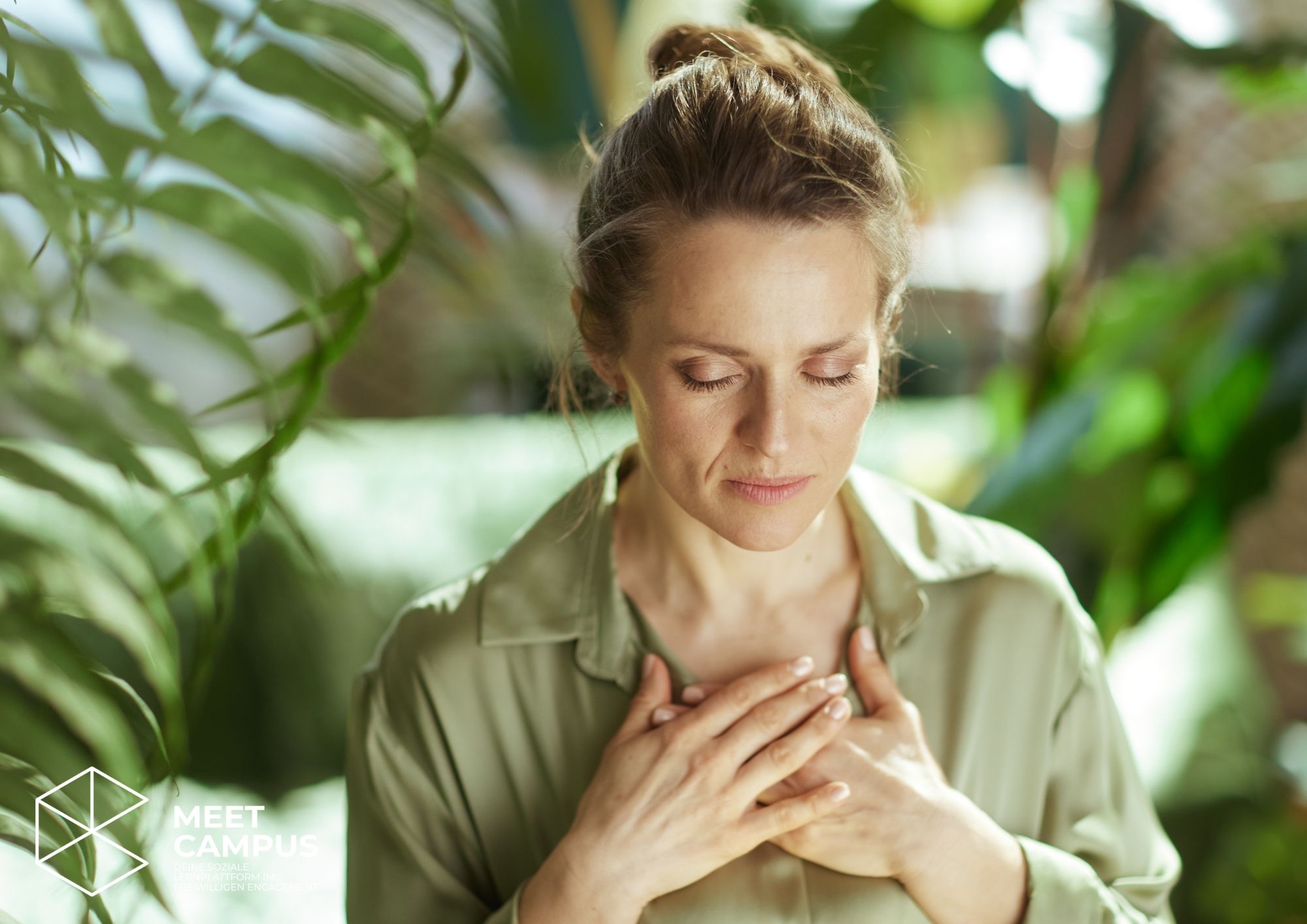Frau mit geschlossenen Augen legt die Hände beruhigend auf die Brust und findet inmitten grüner Pflanzen einen Moment der inneren Ruhe.