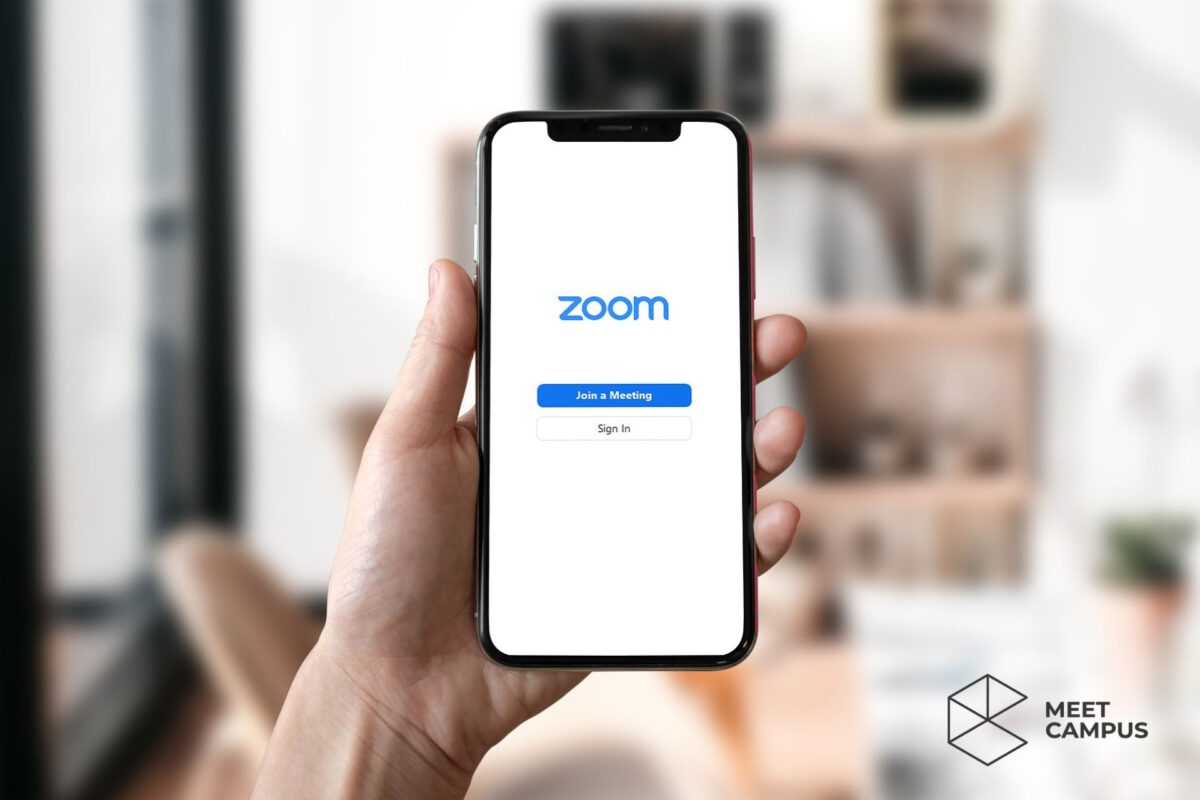 Es wird ein Smartphone in die Kamera gehalten auf dessen Display die Zoom-Seite zu sehen ist