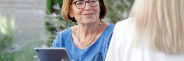 Frau mit Brille im Gespräch mit Tablet in der Hand