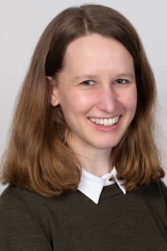 Profilbild von Theresa Kocher, schulterlange Haare, weißer Kragen, dunkler Pulli. Lächelt in die Kamera.