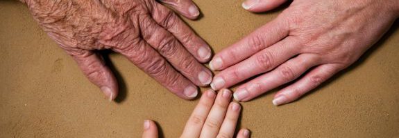 Drei Hände unterschiedlichen Alters liegen nebeneinander auf einer braunen Oberfläche: links eine ältere Hand, in der Mitte eine Kinderhand und rechts eine erwachsene Hand. Unten rechts befindet sich das MEET CAMPUS Logo mit geometrischem Design.