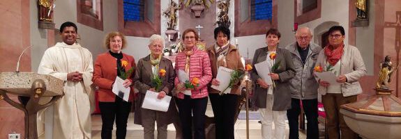 Mehrere Ehrenamtliche Personen stehen in einer Kirche und halten Urkunden und Rosen in der Hand