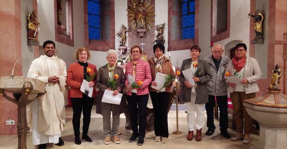 Mehrere Ehrenamtliche Personen stehen in einer Kirche und halten Urkunden und Rosen in der Hand