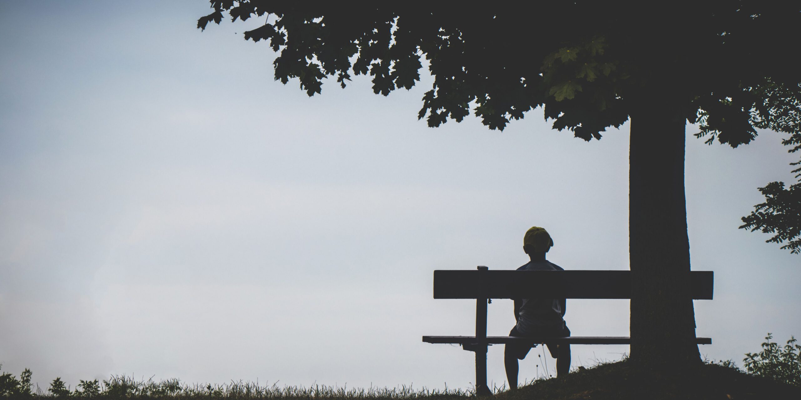 Person sitzt alleine auf einer Bank unter einem Baum, triste Stimmung