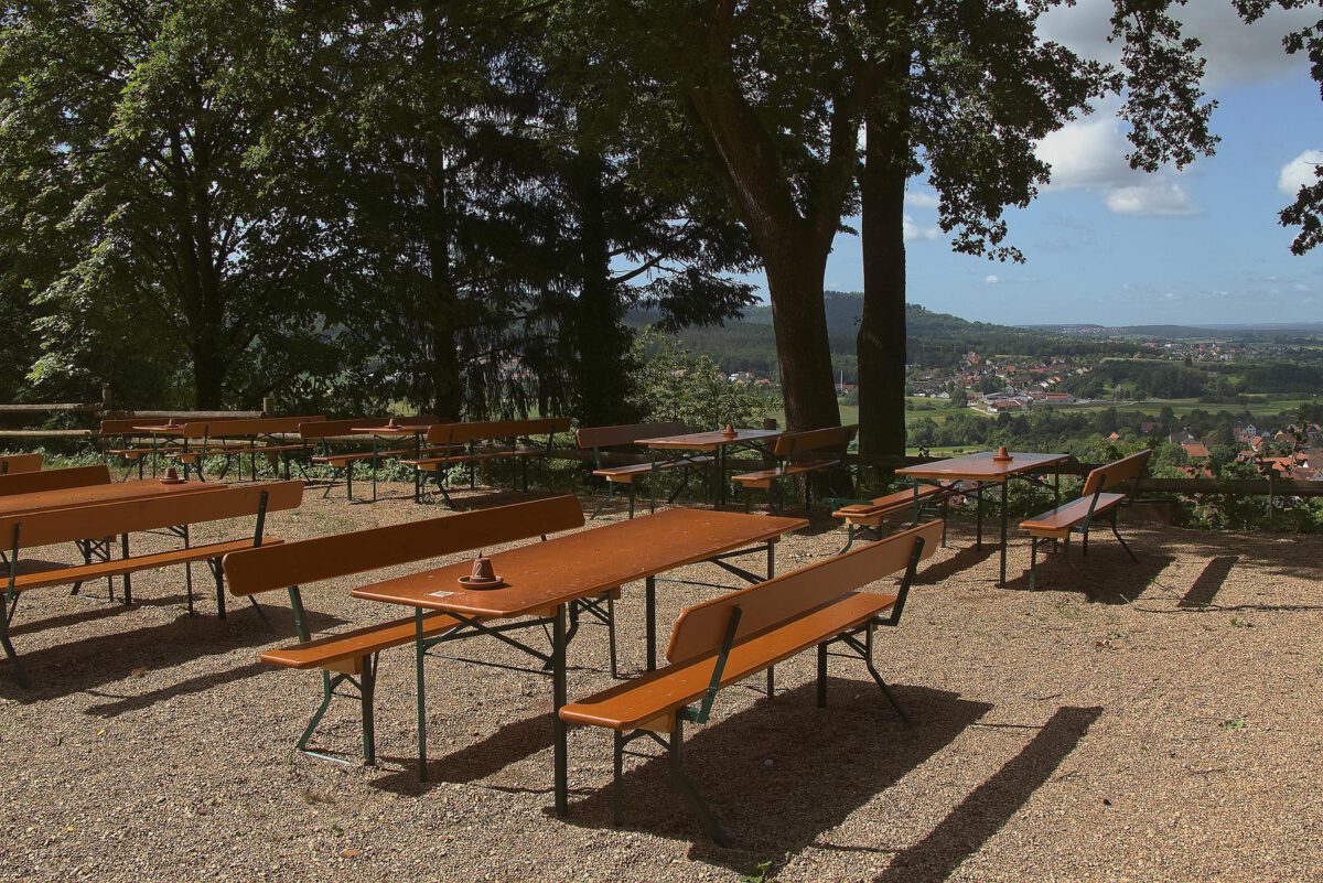 Bierbänke in der Sonne. Im Hintergrund Bäume und Blick über ein Tal.