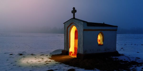 Eine Kapelle im Schnee bei Nacht, die von innen beleuchtet ist