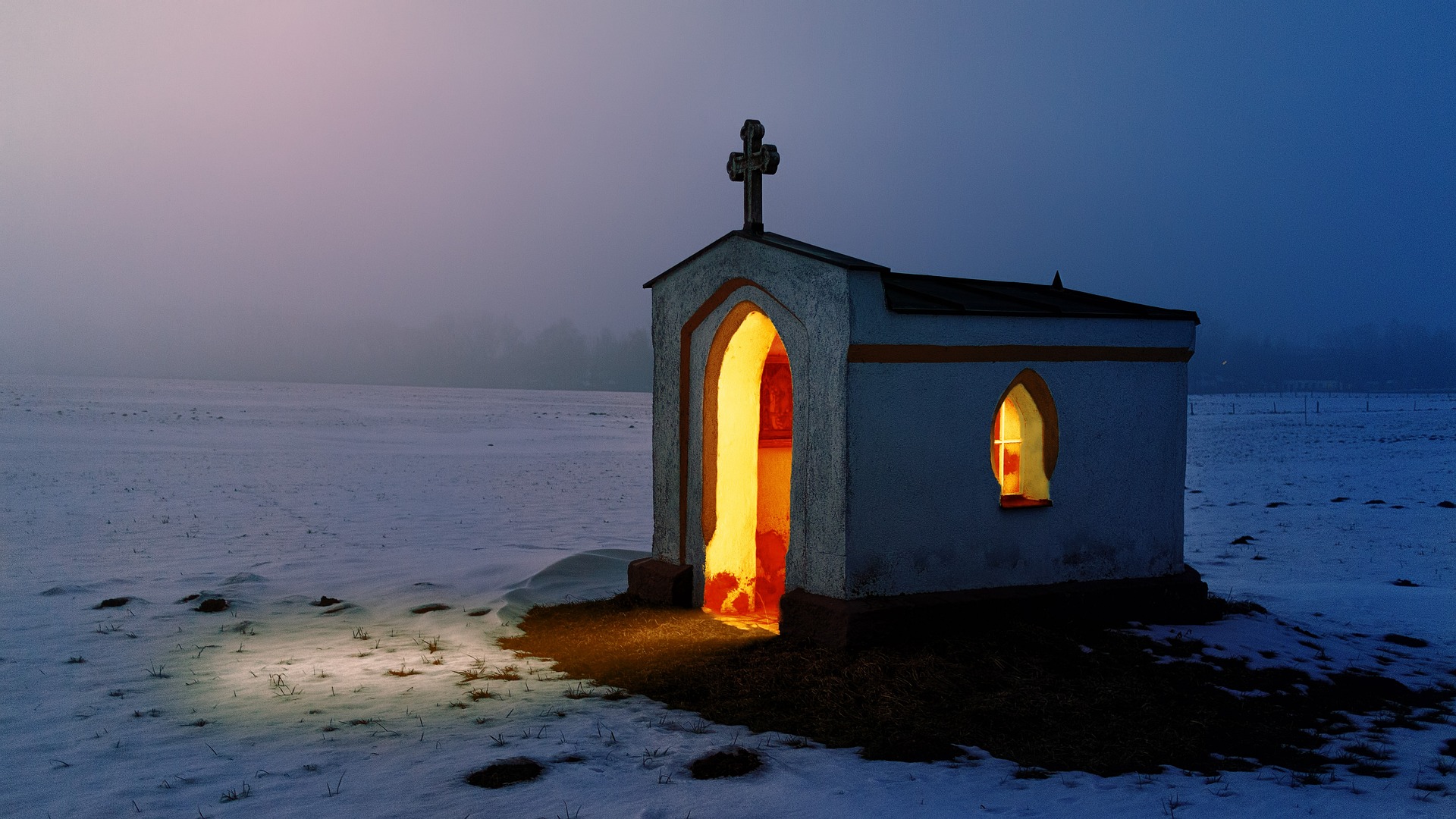 Eine Kapelle im Schnee bei Nacht, die von innen beleuchtet ist