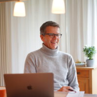 Der MEET CAMPUS Referent Richard Heckert sitzt in einem Wohnzimmer, neben ihm ein aufgeklapptes Notebook.